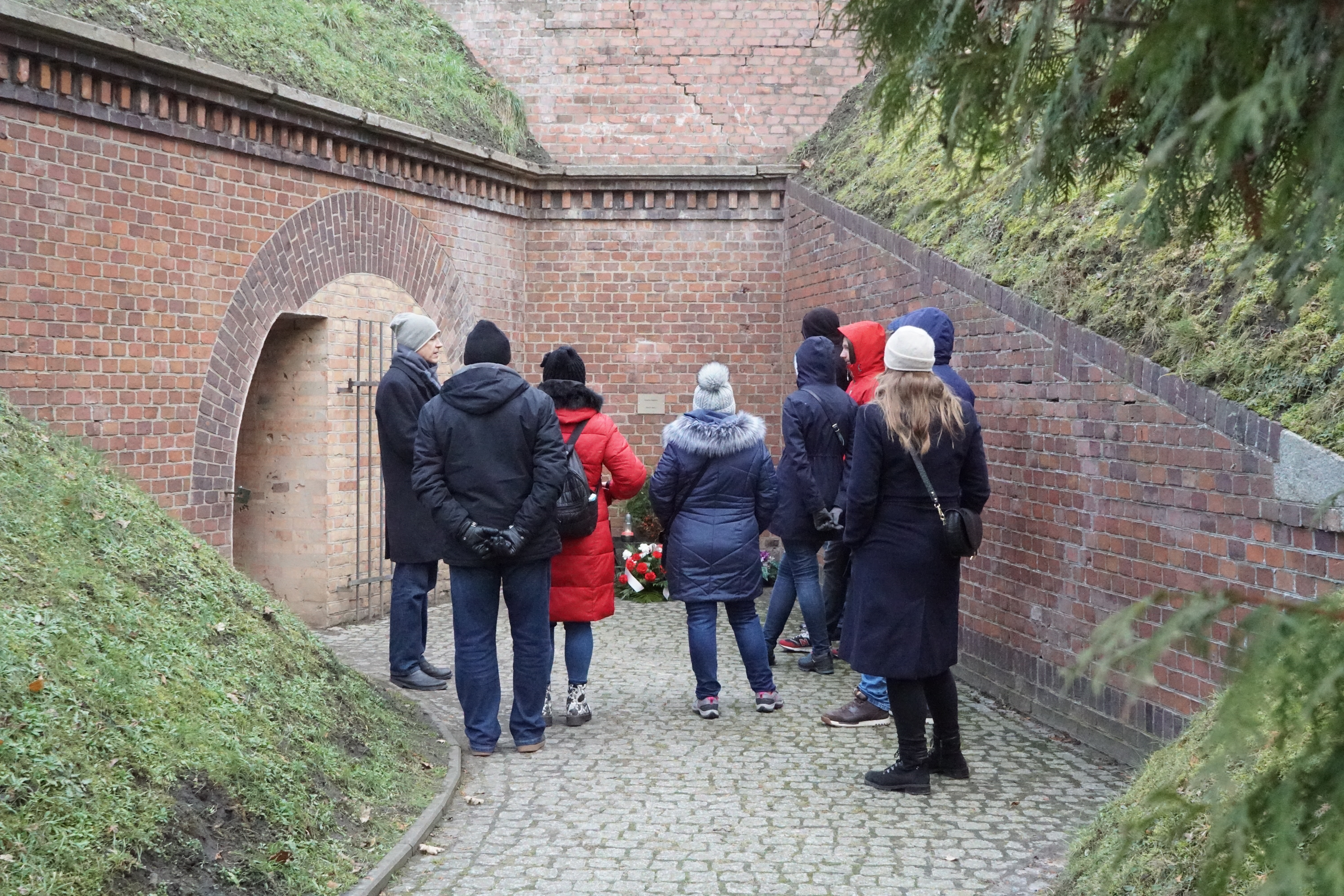 Zwiedzający fort VII przy ścianie śmierci
