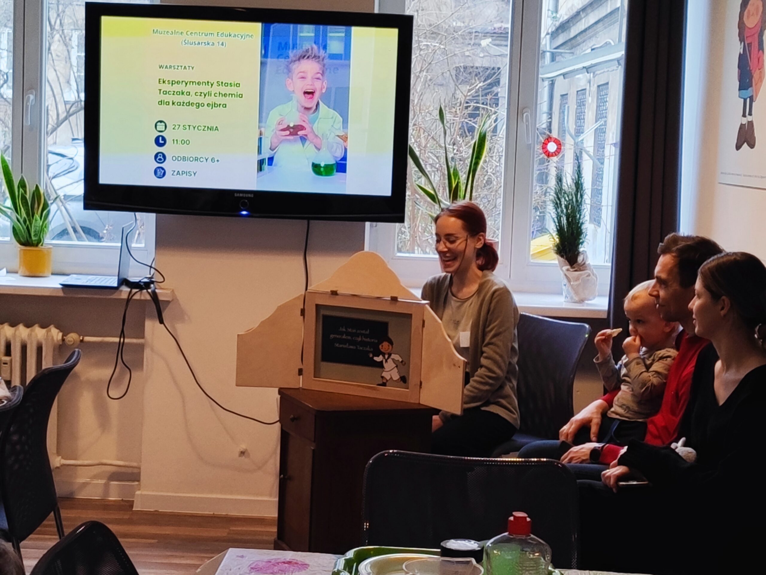 Zdjęcie z warsztatów pod tytułem „Eksperymenty Stasia Taczaka, czyli chemia dla każdego ejbra”. W centrum fotografii widzimy przedstawienie lalek o wokół słuchaczy.