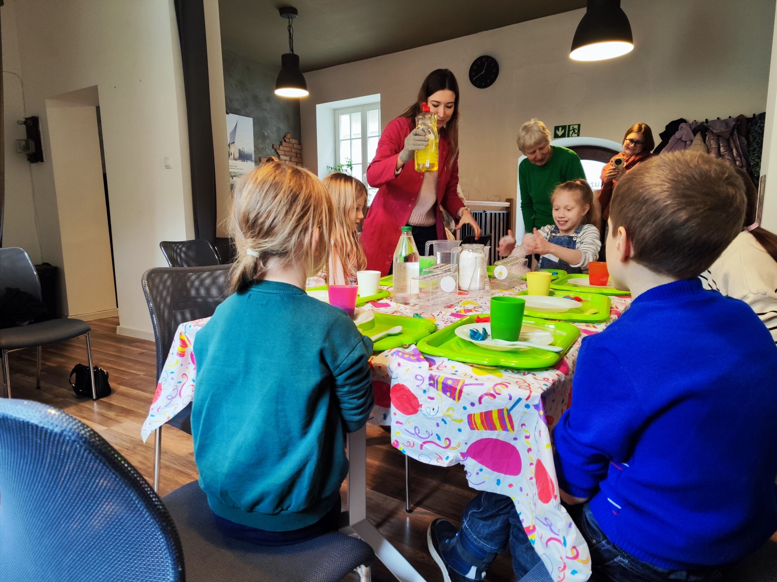 Zdjęcie z warsztatów pod tytułem „Eksperymenty Stasia Taczaka, czyli chemia dla każdego ejbra”. W centrum fotografii widzimy prowadzącą tłumaczącą, dlaczego muszą użyć płynu do mycia naczyń.