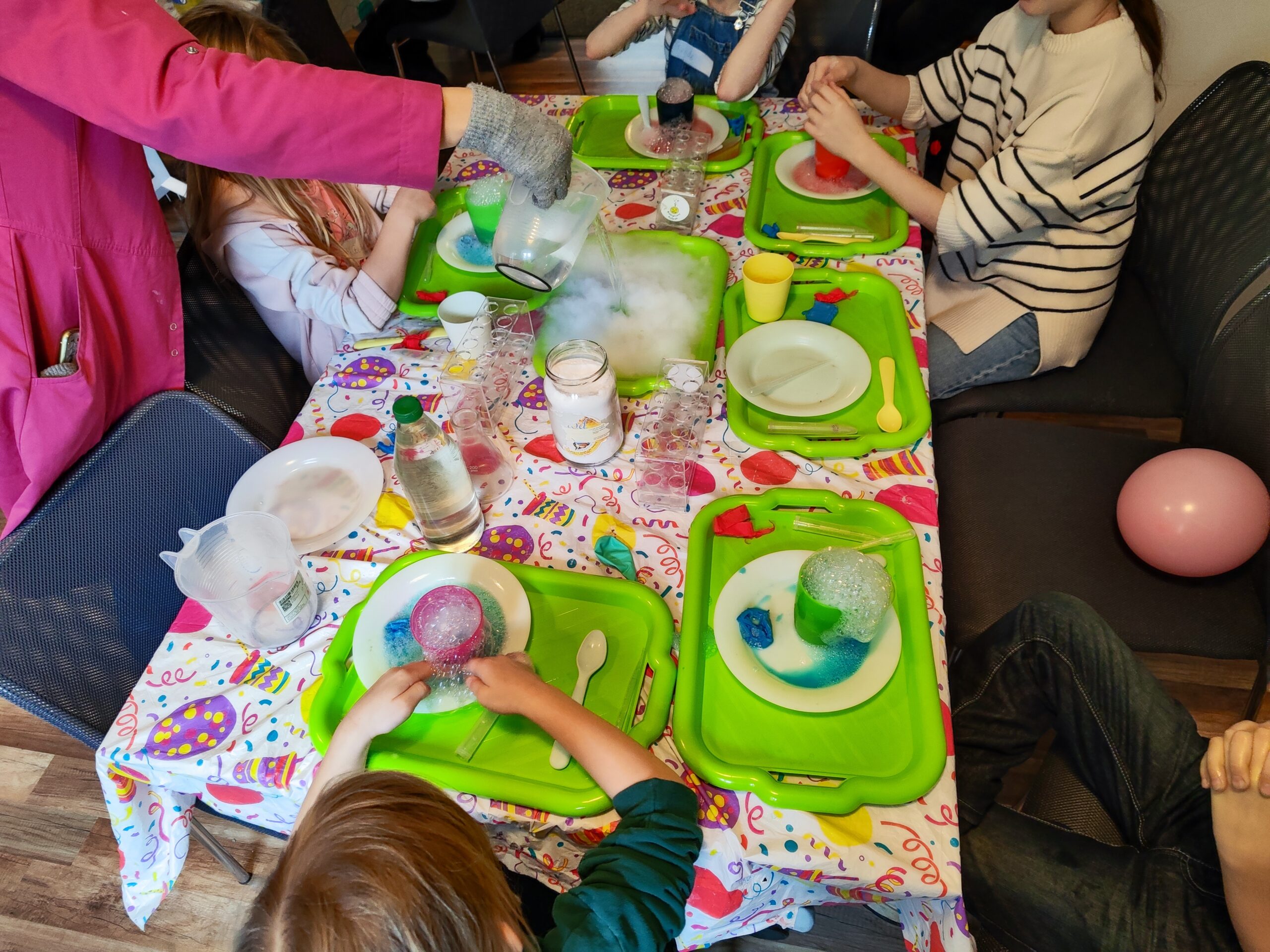 Zdjęcie z warsztatów pod tytułem „Eksperymenty Stasia Taczaka, czyli chemia dla każdego ejbra”. Na fotografii widzimy dzieci z wulkanami i suchy lód, który pod temperaturą dolanej wody wydziela dym.