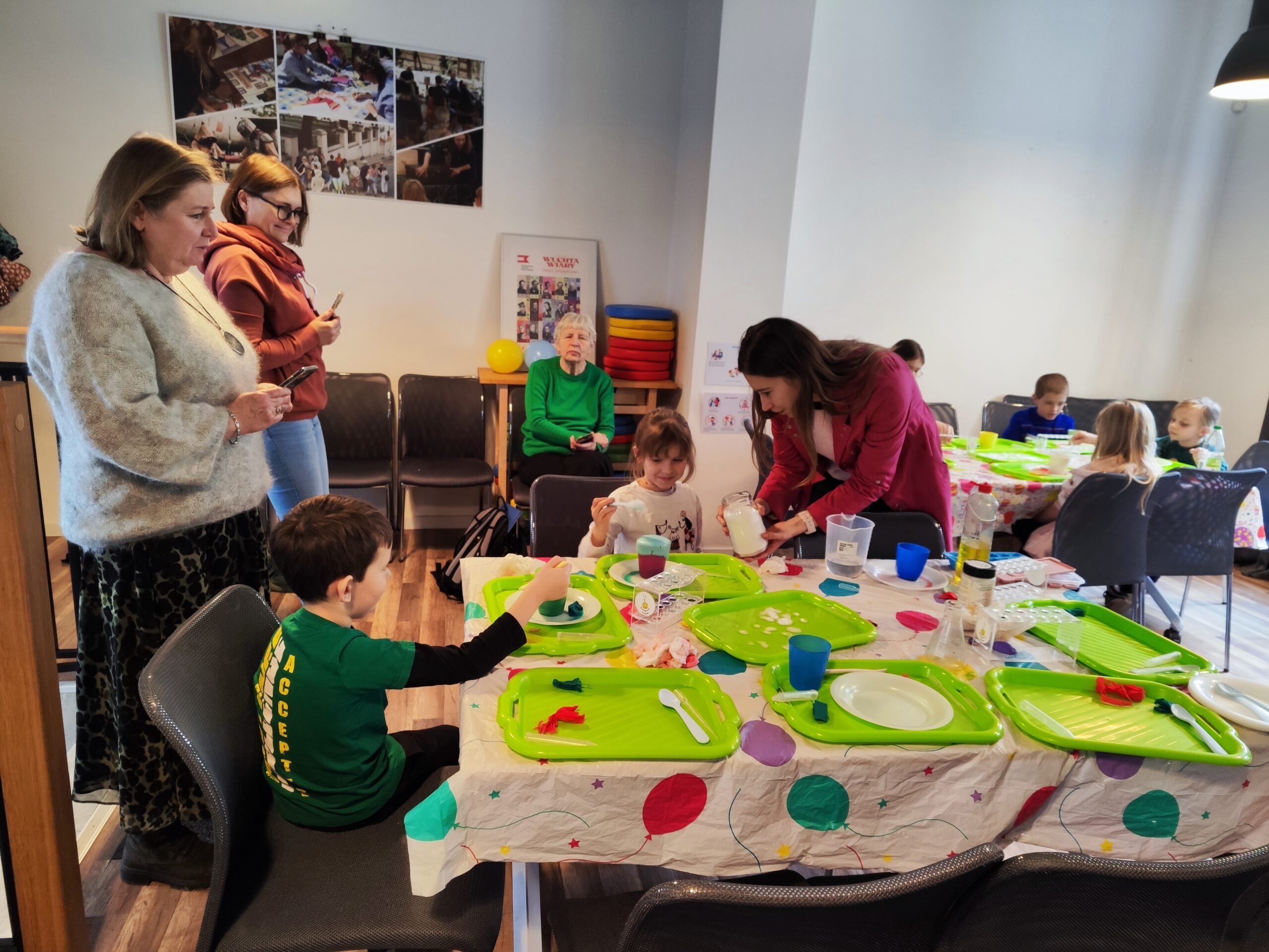 Zdjęcie z warsztatów pod tytułem „Eksperymenty Stasia Taczaka, czyli chemia dla każdego ejbra”. Na fotografii prowadząca pomaga dziewczynce przy eksperymencie z wulkanem.