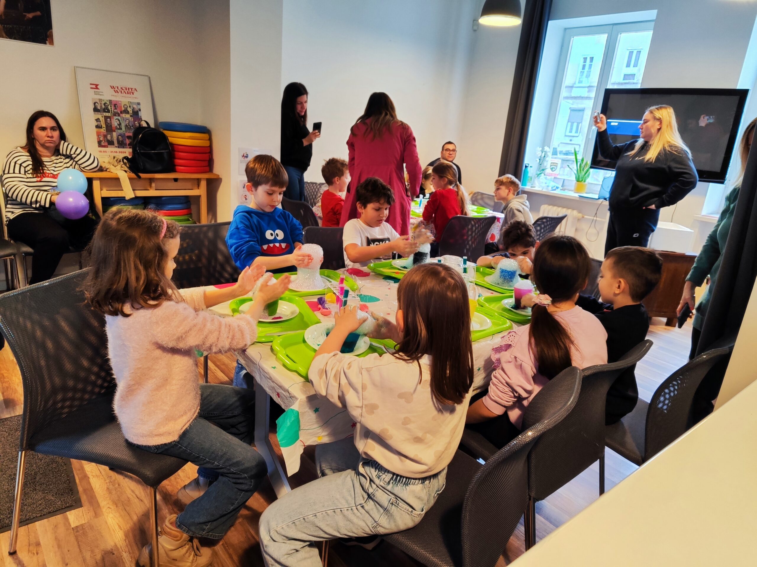 Zdjęcie z warsztatów pod tytułem „Eksperymenty Stasia Taczaka, czyli chemia dla każdego ejbra” Na zdjęciu widzimy grupkę dzieci eksperymentujących z suchym lodem.