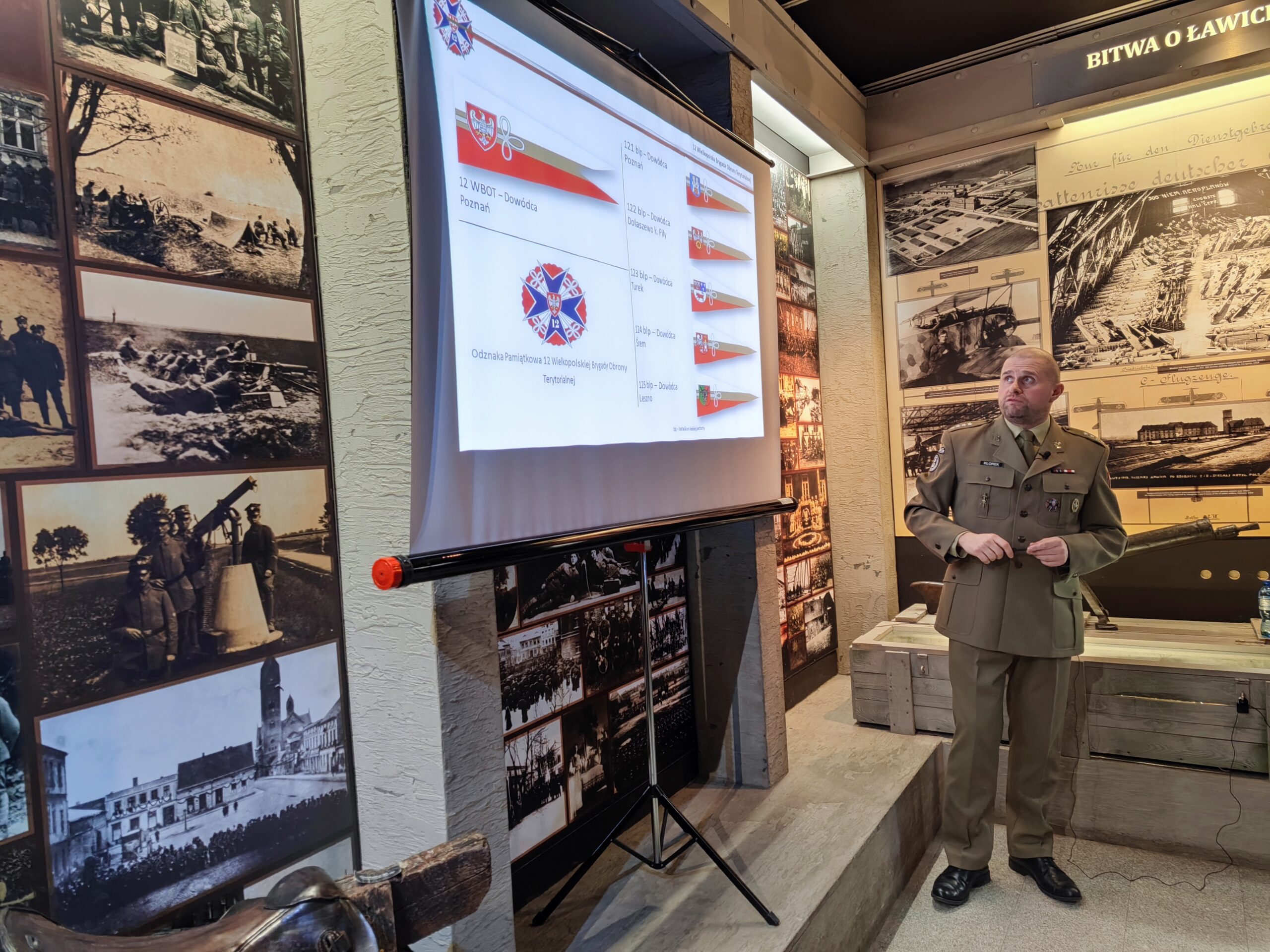 Zdjęcie przedstawia prelekcje w Muzeum Powstania Wielkopolskiego 1918-1919. Prowadzący opowiada o aktualnie wyświetlonym slajdzie prezentacji.