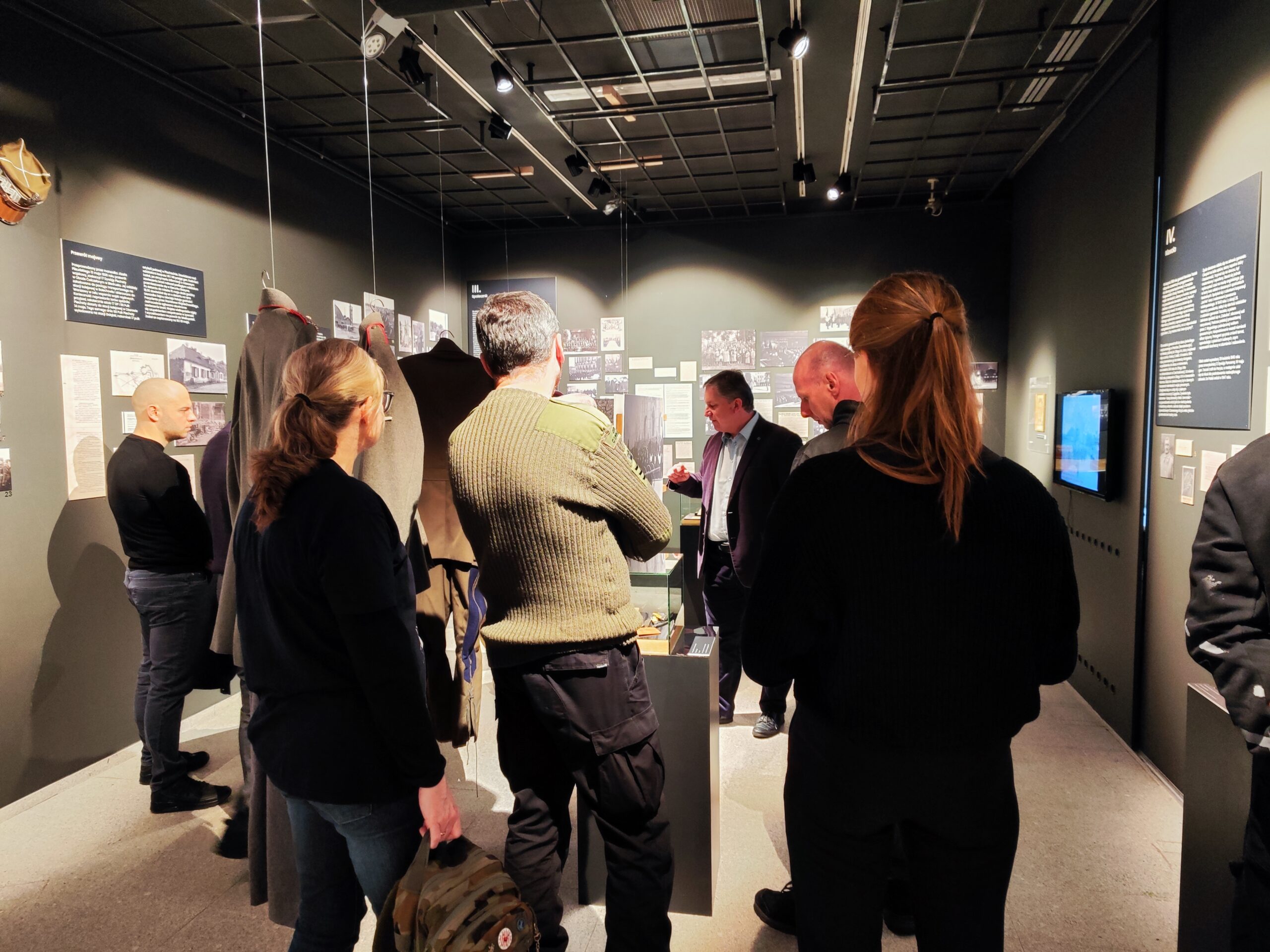 Zdjęcie przedstawia grupę osób zwiedzających wystawę czasową „Generał Stanisław Taczak - naukowiec, dowódca, społecznik” w Muzeum Powstania Wielkopolskiego 1918-1919 z przewodnikiem.