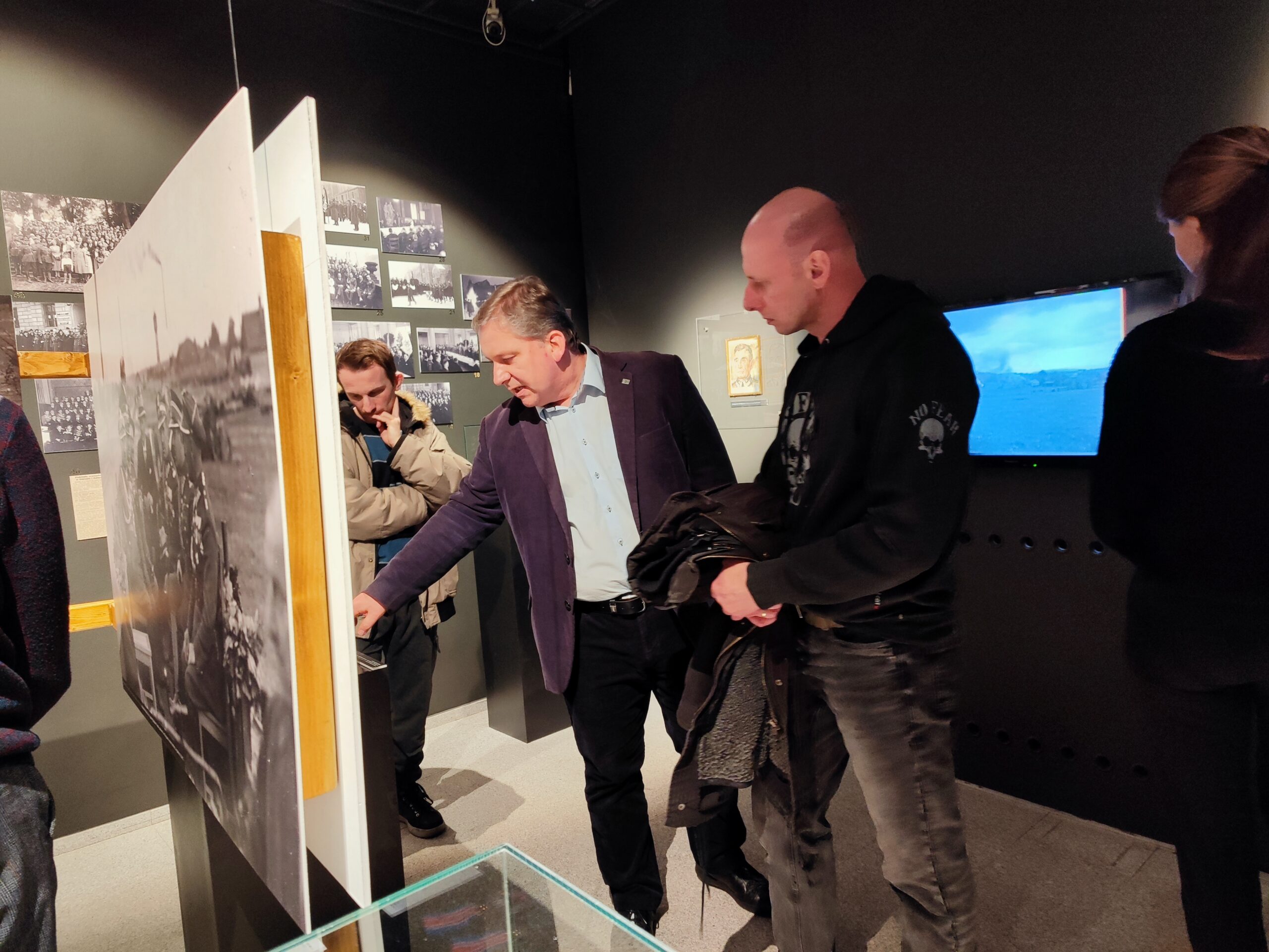 Zdjęcie przedstawia dwie osoby zwiedzające wystawę czasową o Stanisławie Taczaku „Naukowiec, dowódca, społecznik” w Muzeum Powstania Wielkopolskiego 1918-1919. Przewodnik opowiada o zdjęciu.