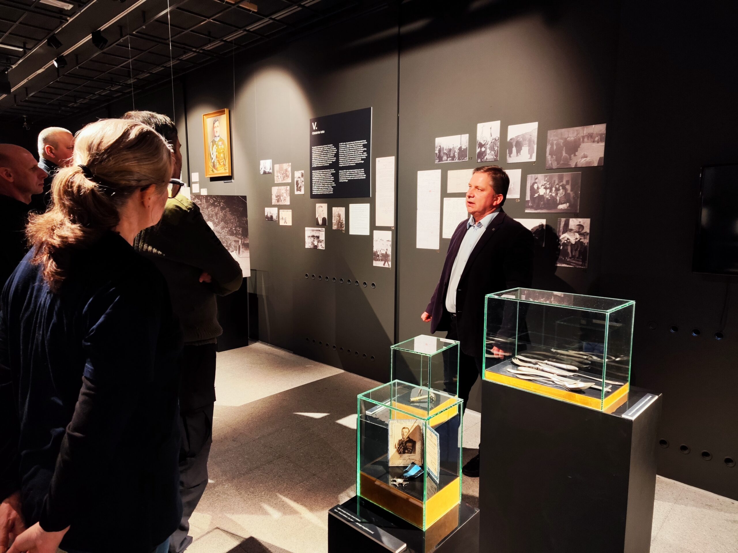 Zdjęcie przedstawia grupę osób zwiedzających wystawę czasową „Generał Stanisław Taczak - naukowiec, dowódca, społecznik” w Muzeum Powstania Wielkopolskiego 1918-1919 z przewodnikiem.