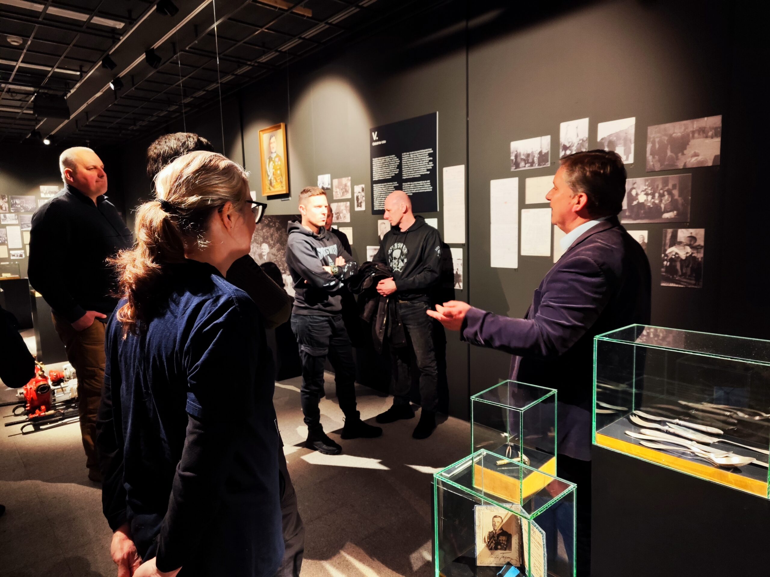 Zdjęcie przedstawia grupę osób zwiedzających wystawę czasową „Generał Stanisław Taczak - naukowiec, dowódca, społecznik” w Muzeum Powstania Wielkopolskiego 1918-1919 z przewodnikiem.