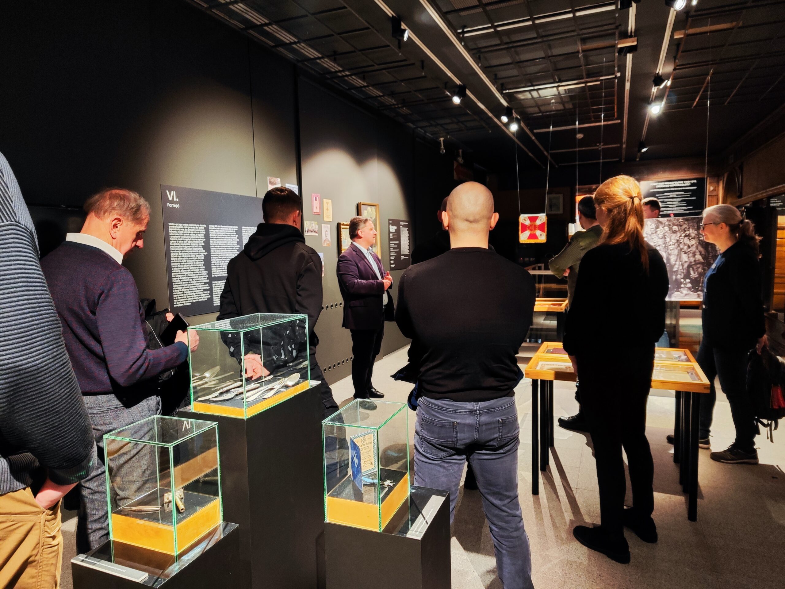 Zdjęcie przedstawia grupę osób zwiedzających wystawę czasową „Generał Stanisław Taczak - naukowiec, dowódca, społecznik” w Muzeum Powstania Wielkopolskiego 1918-1919 z przewodnikiem.